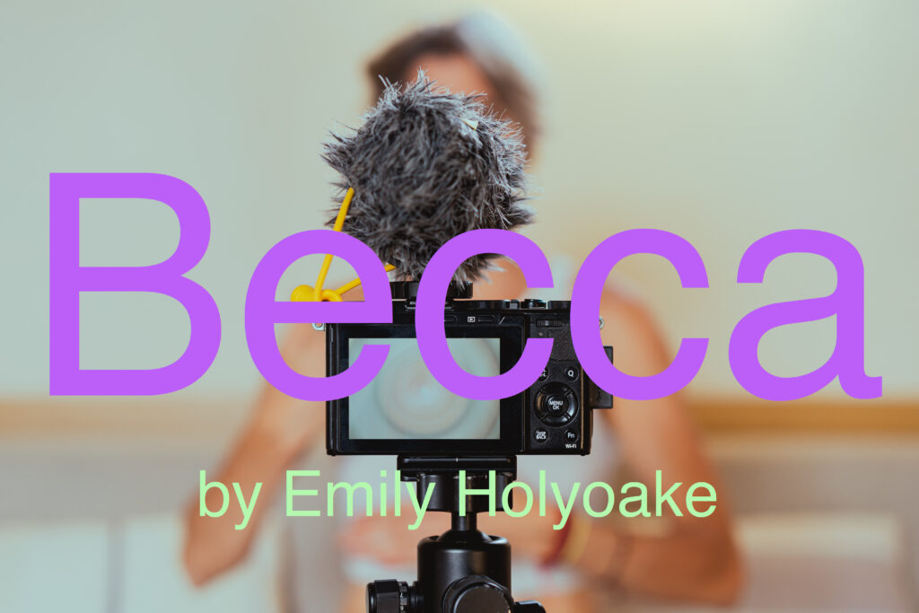 A vlogging camera with a fluffy mic in focus in the foreground, filming a blurry person in the background, with text over the image reading 'Becca by Emily Holyoake'